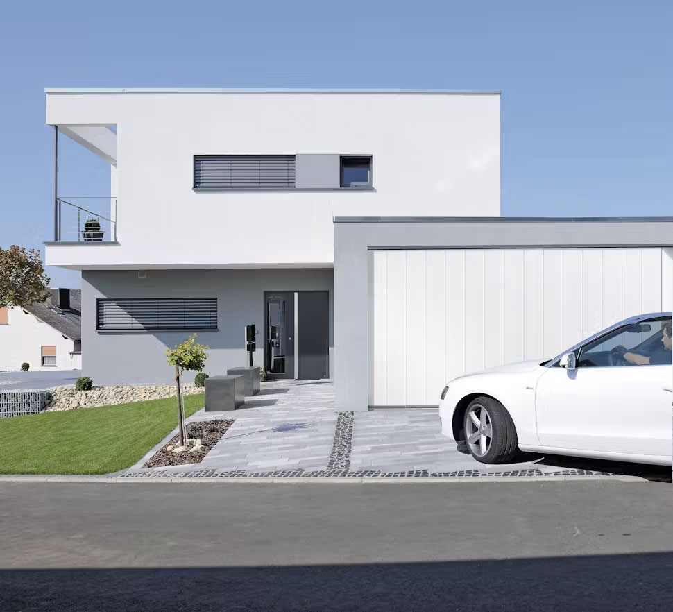 weißes modernes Haus mit weißer Garage und einem anfahrenden weißen Auto